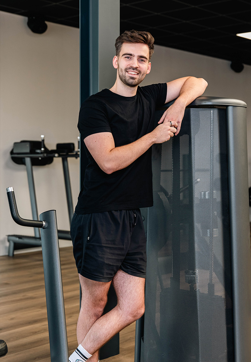 Coach poseert met zijn armen op fitnessapparatuur